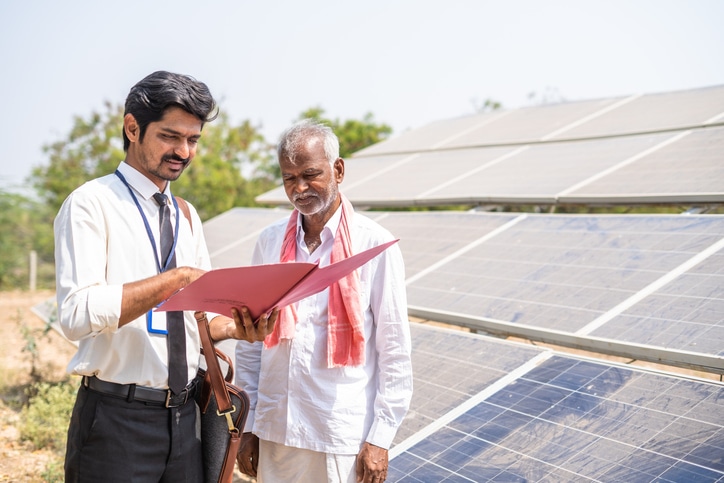 Two Indian men looking at paperwork while standing in front of solar panels